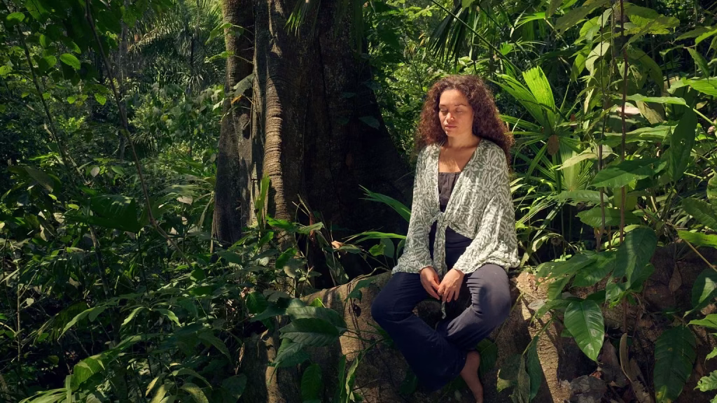 A woman meditating near the roots of an old tree in the middle of a forest.