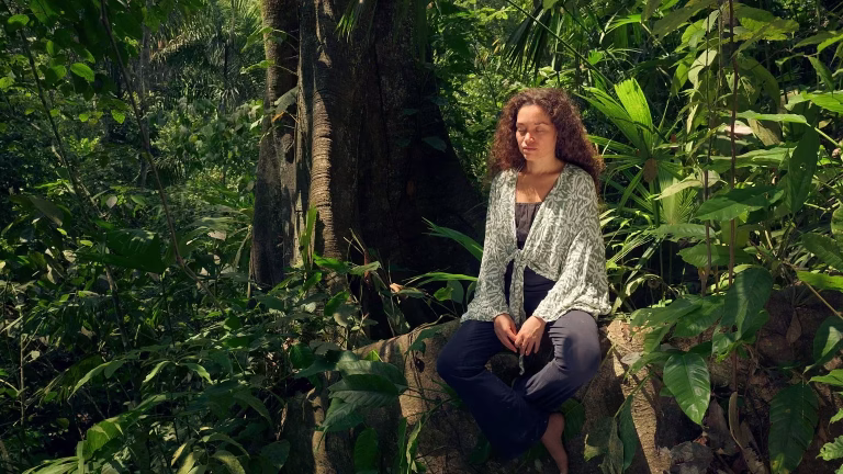 A woman meditating near the roots of an old tree in the middle of a forest.